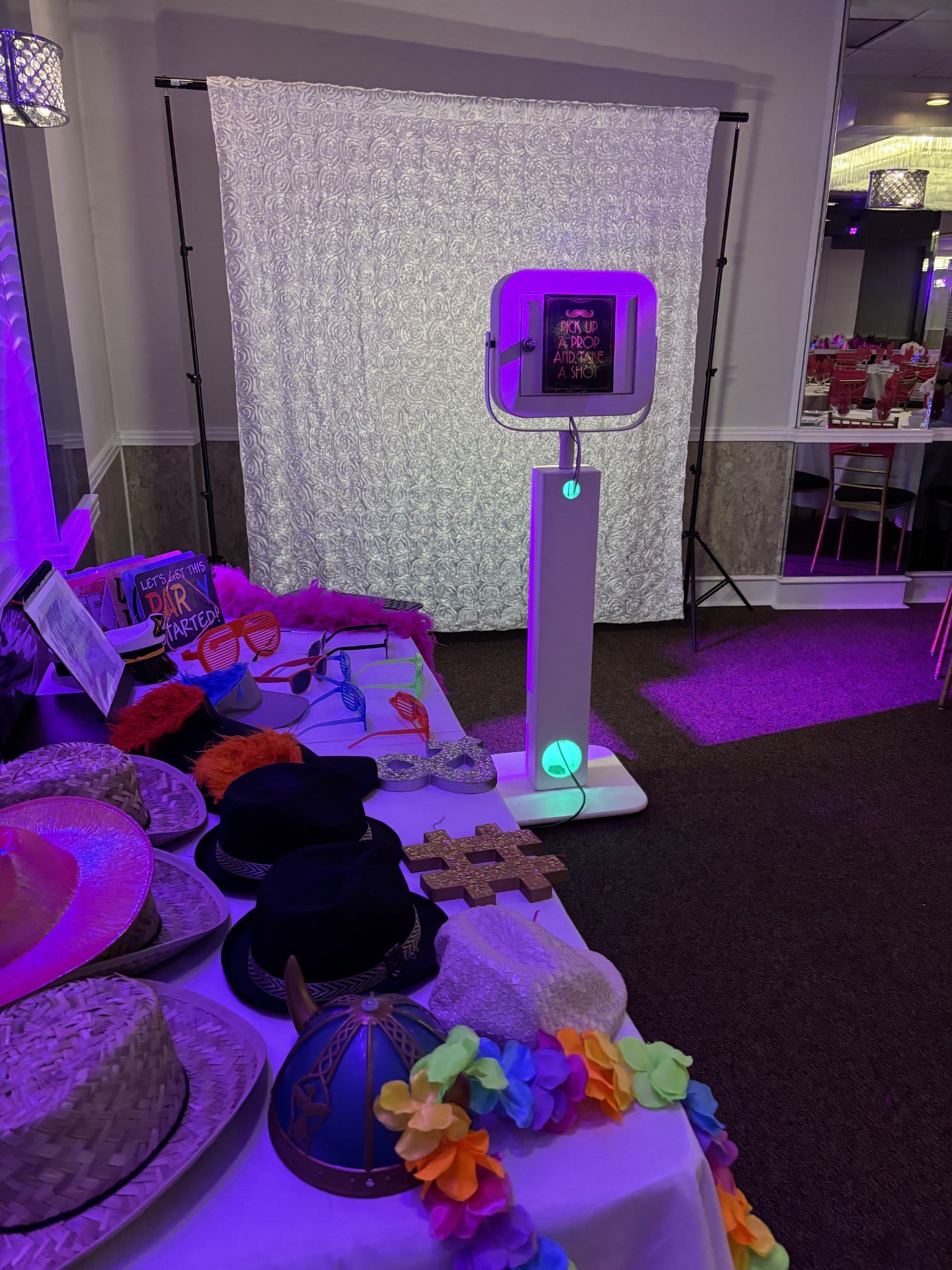 Selfie booth kiosk set up at a venue with white backdrop and props